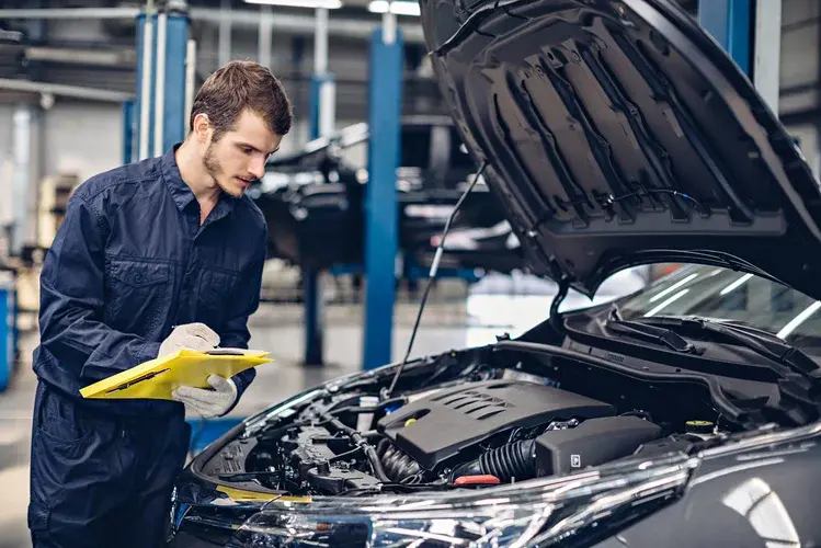 Mechanic with clipboard looking into car engine bay